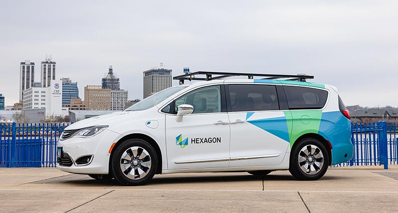 White Chrysler Pacifica for Hexagon branding in front of a cityscape